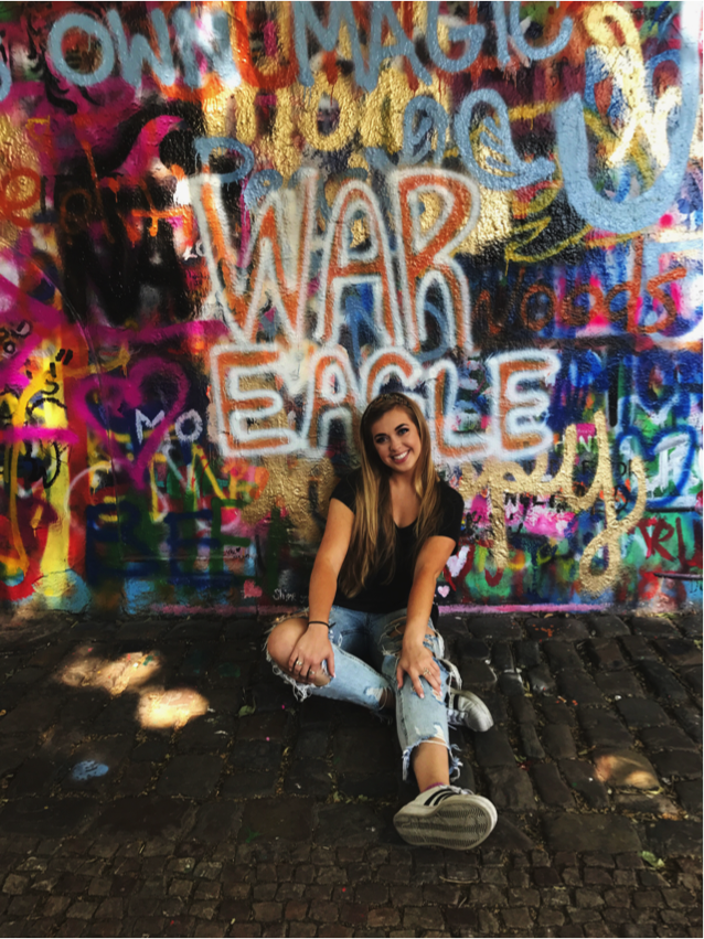 Auburn student abroad in Prague sitting and leaning against a graffiti laden wall underneath the words "War Eagle"